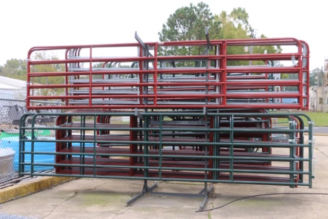 Stacked red and green metal barriers are placed on a concrete surface outdoors. The arrangement creates a grid-like pattern, with trees and fencing visible behind.
