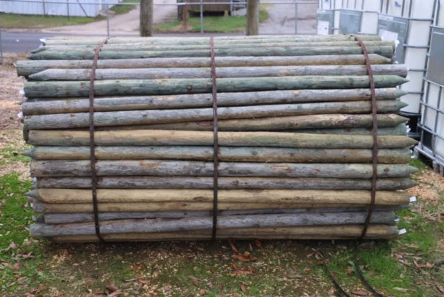 A stack of wooden poles bound together with metal bands, resting on a grassy area. The wood appears weathered and stacked neatly in an outdoor setting.
